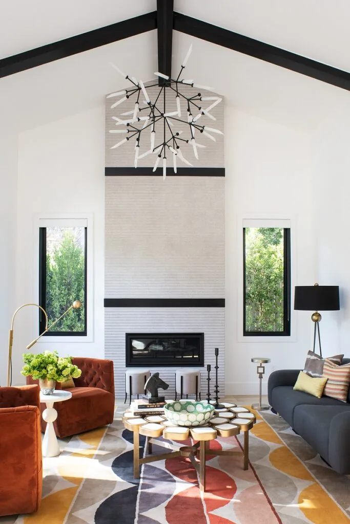 A double-height living room with a stone fireplace wall, rust velvet chairs and a patterned rug