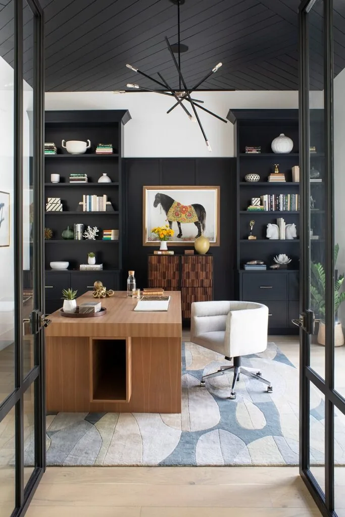 A home office with black lacquered shelving, a walnut desk and steel-framed glass doors
